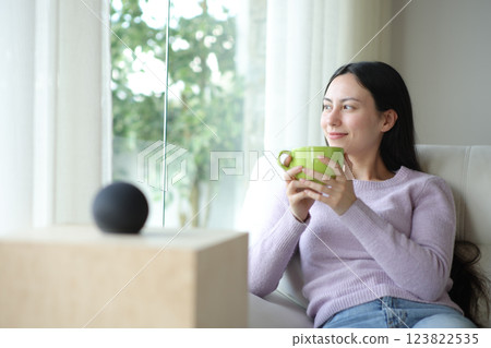 Relaxed asian woman drinking beside a smart speaker 123822535
