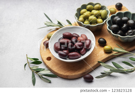 Kalamata, green and black olives displayed on wooden cutting board with olive branches Kalamata, green and black olives displayed on wooden cutting board with olive branches 123823128