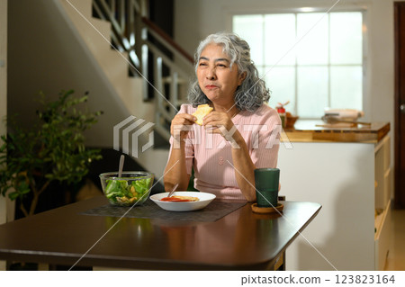 Happy senior woman with gray curly hair having a nutritious lunch at a dining table 123823164