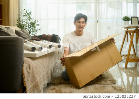 Young man unpacking parts of a new table from cardboard box preparing for the assembly process in a living room Young man unpacking parts of a new table from cardboard box preparing for the assembly process in a living room 123823227