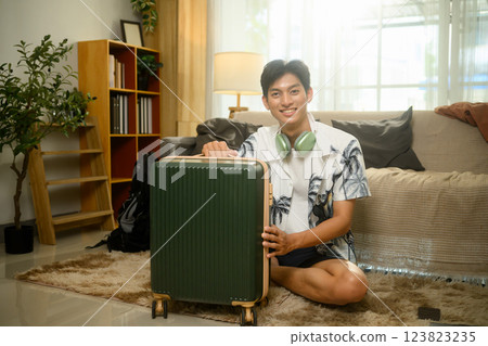 Cheerful young asian man packing his suitcase for a summer trip Cheerful young asian man packing his suitcase for a summer trip 123823235