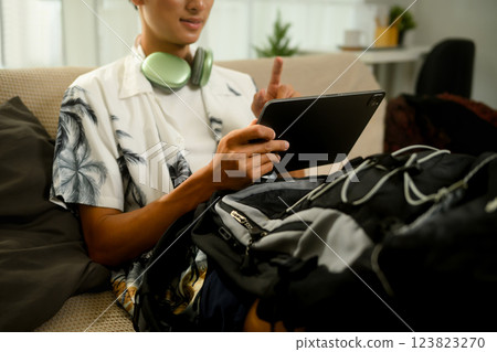 Smiling asian man booking or checking travel plans on digital tablet before summer trip 123823270