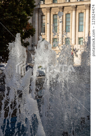 Water fountain splashes create dynamic scenes in Bucharest, Romania, with historic architecture in the background during a sunny afternoon 123824474
