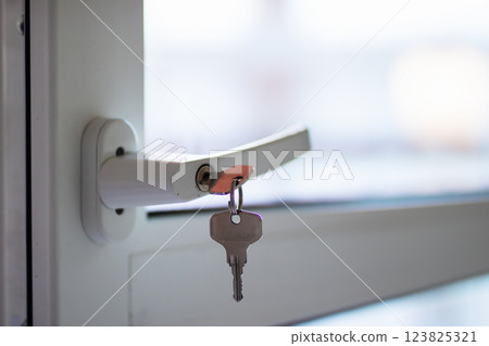 Two shiny keys are hanging stylishly from a white door handle Two shiny keys are hanging stylishly from a white door handle 123825321