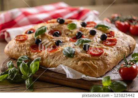 Focaccia - Italian Bread with tomatoes basil leaves olives and olive oil on cutting board Focaccia - Italian Bread with tomatoes basil leaves olives and olive oil on cutting board 123825442