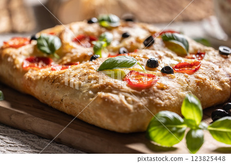 Focaccia - Italian Bread with tomatoes basil leaves olives and olive oil on cutting board 123825448