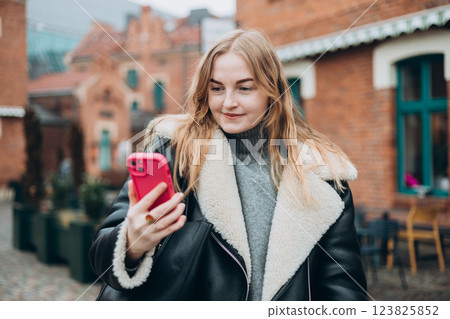 Laughing young woman taking selfie on the urban background. Cute beautiful woman using mobile phone. 30s girl recording self video, talking on online call 123825852