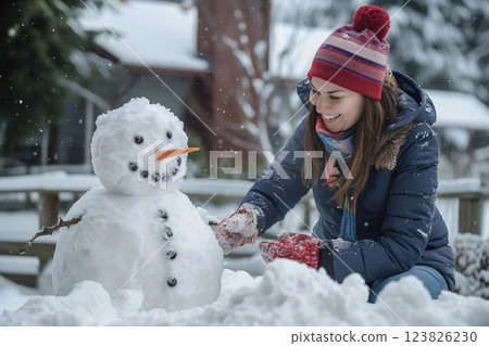Woman happily building a snowman with her daughter in the backyard on a snowy winter day, enjoying the cold weather and togetherness of family bonding during the festive season 123826230