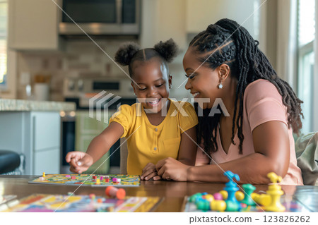 Mother and her daughter are smiling while playing board games at their dining room table 123826262