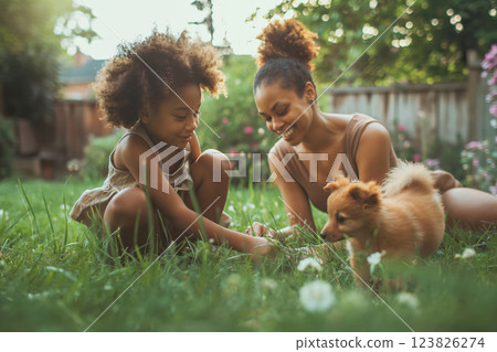 Mother and daughter are crouching in the grass, playing with a puppy in their backyard on a sunny day 123826274