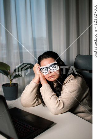 Tired Caucasian woman freelancer feeling stressed from work problems. Irritation burnout. Painted eyes on adhesive notes glued to face. Not having enough sleep Tired Caucasian woman freelancer feeling stressed from work problems. Irritation burnout. Painted eyes on adhesive notes glued to face. Not having enough sleep 123827016