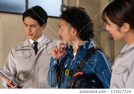 Three people, a man and a woman in work clothes, looking at drawings and having a meeting Three people, a man and a woman in work clothes, looking at drawings and having a meeting 123827329