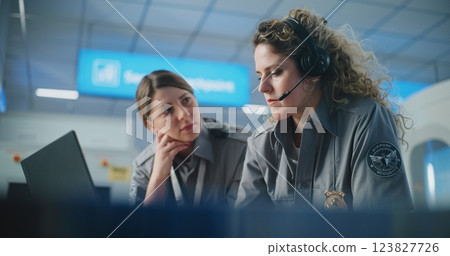 Airport Security Checkpoint: Two Female Security Officers in Headset Using Laptop Computer, Talking 123827726