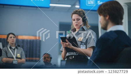 Female TSA Officer with Tablet Computer Wearing Headset Instructs Airport Staff Female TSA Officer with Tablet Computer Wearing Headset Instructs Airport Staff 123827729
