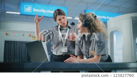 Female TSA Officer Wearing Headset Uses Laptop, Discusses Security Issues with Colleague 123827760