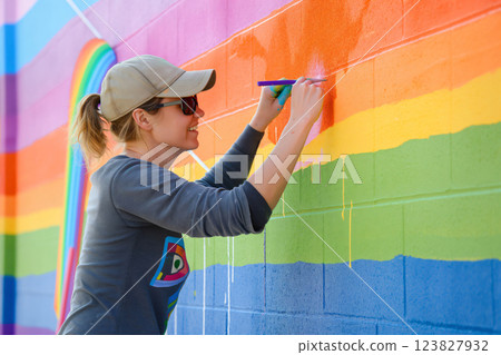 Artist skillfully paints a vibrant rainbow flag mural on a building wall, celebrating pride and diversity in the urban landscape 123827932