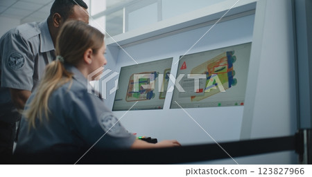 Two TSA Workers Controlling X-ray Scanning of Suitcase on Computer Monitors 123827966