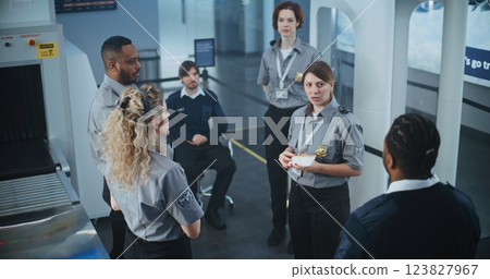 Female Security Officer Holding Boarding Pass, Explaining Procedures to Team of Workers 123827967