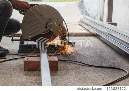 Metal worker cutting metal tube by electric grinding machine. 123828122