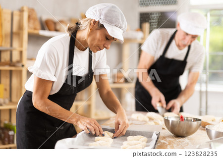 Elderly man and woman molding and cutting pieces of dough 123828235