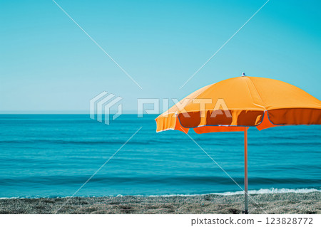 Striking orange beach umbrella stands out against the tranquil blue backdrop of the ocean under a clear sunny sky Striking orange beach umbrella stands out against the tranquil blue backdrop of the ocean under a clear sunny sky 123828772