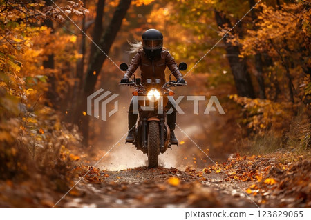 Woman rides her motorcycle on a leafstrewn path through a forest, surrounded by the warm colors of autumn 123829065