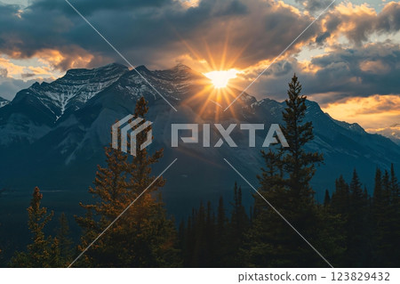 Dramatic sunrise casting golden rays over snowcapped mountains with silhouetted pine trees in the foreground 123829432