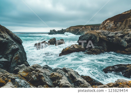 Atmospheric photo capturing the dynamic interaction between waves and rocky cliffs under a dramatic overcast sky at a secluded beach 123829454