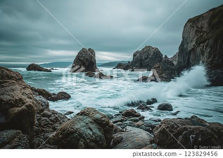 Serene coastal landscape featuring rugged cliffs, a stony beach, and waves breaking against rocks under a dramatic sky 123829456