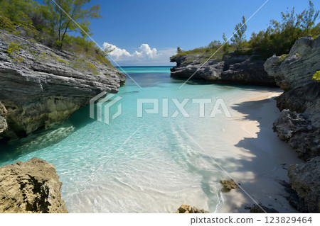 Serene, secluded cove with crystal-clear turquoise waters, framed by rugged rocks and lush greenery under a bright blue sky 123829464