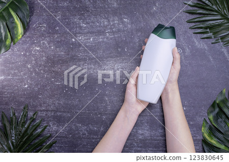 Female hands holding shower gel bottle on gray background with leaves Female hands holding shower gel bottle on gray background with leaves 123830645