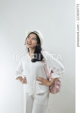 Portrait of a beautiful young woman in hat, stylish white shirt hands on waist and carrying ping bag posing happy, isolated on white background 123830772