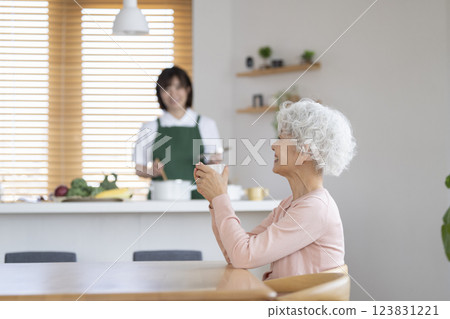 一位 30 多歲的女性在廚房做飯，一位老年女性在餐桌旁喝茶 家事服務圖片 123831221