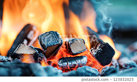 Burning wood with bright orange flames and glowing embers, showing cracked charcoal texture and intense heat in a close-up, dramatic composition. 123832025