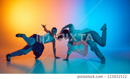 Young women dancing hip hop in casual outfits against gradient studio background in neon light. Young women dancing hip hop in casual outfits against gradient studio background in neon light. 123832512