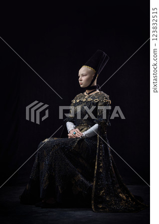 Bald young woman in renaissance dress sitting with serene expression, embodying ethereal elegance and timeless beauty against dark vintage background. 123832515