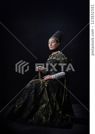 Elder noblewoman in renaissance dress holding golden necklace with cross, gazing forward with serene expression against dark background. Elder noblewoman in renaissance dress holding golden necklace with cross, gazing forward with serene expression against dark background. 123832581