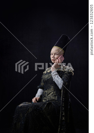 Medieval woman dressed elegant, renaissance style clothes talking on smartphone against dark vintage background. Medieval woman dressed elegant, renaissance style clothes talking on smartphone against dark vintage background. 123832605