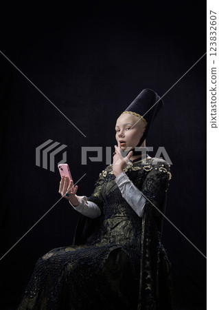 Young woman, with surprised expression, dressed renaissance style outfit and using modern smartphone against dark vintage background. Young woman, with surprised expression, dressed renaissance style outfit and using modern smartphone against dark vintage background. 123832607