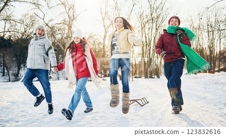 Group of friends joyfully jumping in snow, sharing playful winter moment together in public park cowered with snow. 123832616