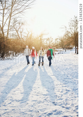 Group of four friends walks through snowy park, chatting and enjoying winter landscape in sunny, cold park. Group of four friends walks through snowy park, chatting and enjoying winter landscape in sunny, cold park. 123832619