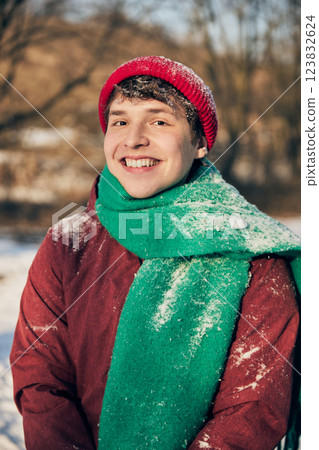 Portrait of young man in red jacket and green scarf wipes snow from forehead, enjoying crisp winter air. Portrait of young man in red jacket and green scarf wipes snow from forehead, enjoying crisp winter air. 123832624