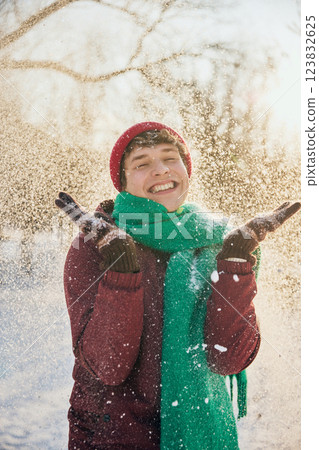 Young man in red hat and green scarf with snow-covered jacket smiles warmly in winter scenery. 123832625