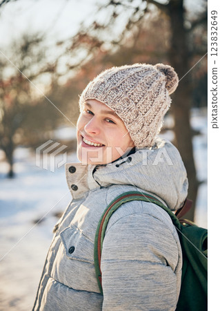 Happy, smiling young man dressed cozy., warm winter clothes looking at camera, sharing his excitement, while he walking in snowy park on sunny winter day. Happy, smiling young man dressed cozy., warm winter clothes looking at camera, sharing his excitement, while he walking in snowy park on sunny winter day. 123832649