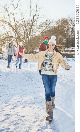 Group of young happy people, men and women, dressed stylish warm clothes, walking among snowy park on sunny winter day, sharing funny moments. 123832653
