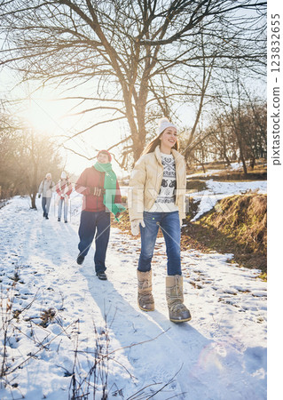 Group of young happy people, men and women, walking among snowy park on sunny winter day, dressed stylish warm clothes. Group of young happy people, men and women, walking among snowy park on sunny winter day, dressed stylish warm clothes. 123832655