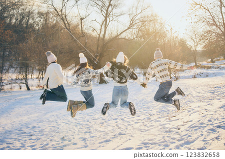 Smiling friends, men and women, jumping with excitement, fun and joy, tossing snow in air, celebrating winter outdoors. 123832658