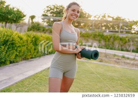 A Joyful Young Woman Embracing Wellness with a Yoga Mat in a Beautiful Outdoor Setting 123832659