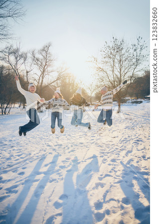 Smiling friends, men and women, jumping with excitement, fun and joy, tossing snow in air, celebrating winter outdoors. 123832660