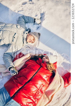 Man and woman resting on snowy ground, laughing together, feeling relaxed in peaceful winter landscape. 123832724
